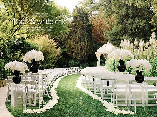 a black and white chic wedding ceremony with white chairs on grass with 4 bouquets of white flowers 